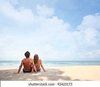 Young couple sitting on a tropical sandy beach