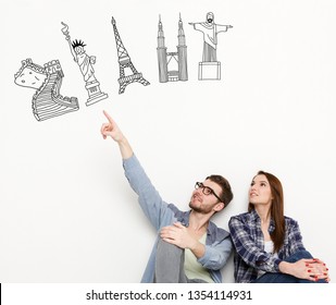 Young couple sitting white background   looking up at tourist attractions drawn above their heads  Choose your travel concept