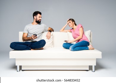 Young Couple Sitting On White Couch And Using Smartphones Isolated On Grey