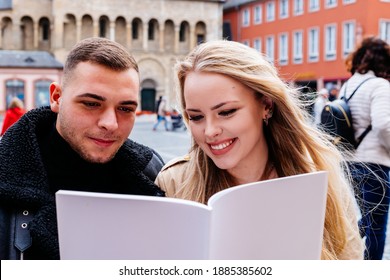 Young Couple Sitting Outside In Cafe Happily Reading Magazine With Blank Cover As Mock Up.