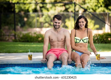 Young couple sitting at poolside on a sunny day - Powered by Shutterstock