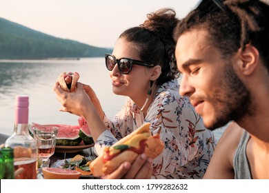 Young Couple Sitting At The Table Eating Hot Dogs On The Nature Outdoors