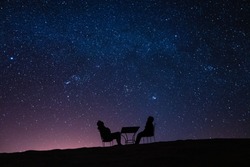 Jeune Couple Assis à Une Table Sur Une Dune Du Désert En Parlant, En Se Relaxant Et En Observant Les étoiles Et La Voie Lactée Au-dessus D'eux