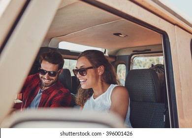 Young couple sitting in their car during roadtrip. Young man and woman wearing sunglasses sitting inside the car and smiling. - Powered by Shutterstock