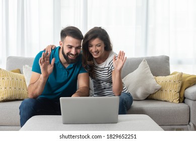 Young couple sitting in their living room with laptop waving to their marital therapist after successful online therapy  and saved marriage  