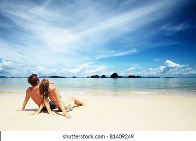 Young couple sitting together on a sand by sea and looking to a horizon