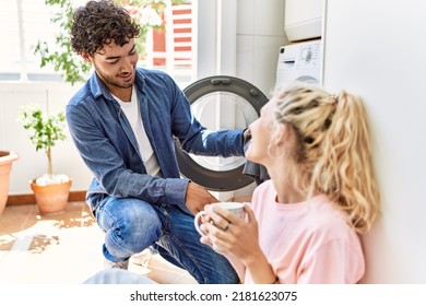 Young Couple Smiling Happy Drinking Coffee While Doing Laundry At Home.