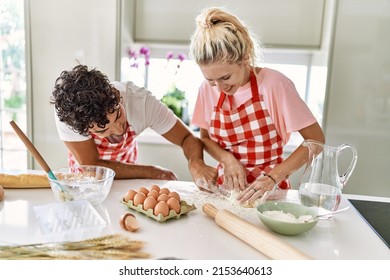 Young couple smiling happy kneading dough with hands at kitchen.