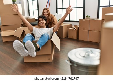 Young Couple Smiling Happy Playing With Cardboard Box As A Car At New Home.