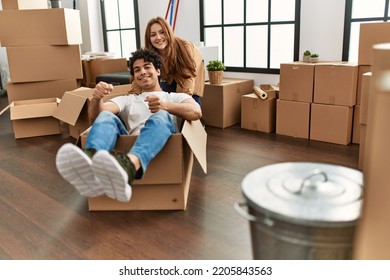 Young Couple Smiling Happy Playing With Cardboard Box As A Car At New Home.