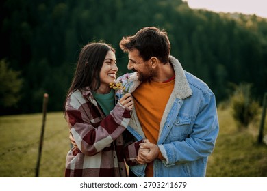 Young couple smiling and hugging while exchanging a bouquet of wildflowers in nature