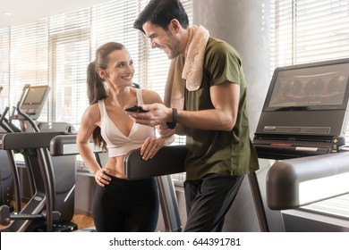 Young couple smiling while communicating on the mobile phone during break at the fitness club - Powered by Shutterstock