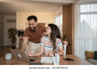 Young couple smiling while using a laptop for online banking, managing finances, shopping online, and connecting with family through video calls
