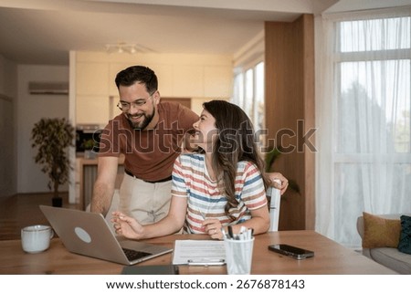 Young couple smiling while using a laptop for online banking, managing finances, shopping online, and connecting with family through video calls