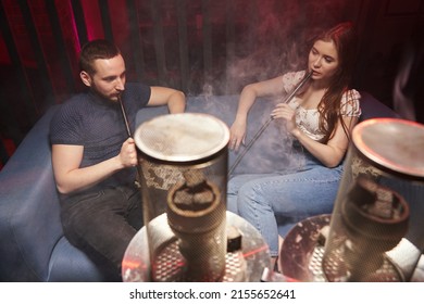a young couple smokes a hookah in an atmospheric hookah lounge in a relaxed atmosphere, in front of a hookah with a protective screen on the coals