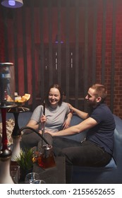 a young couple smokes a hookah in an atmospheric hookah lounge and laugh merrily. rest, relaxation, friendship