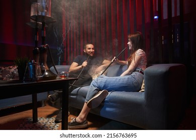 young couple smoking hookah in atmospheric hookah bar. sit freely on sofas, talking, laughing and exhaling smoke