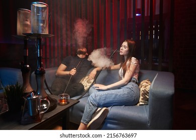 young couple smoking hookah in atmospheric hookah bar. sit freely on sofas and blow smoke