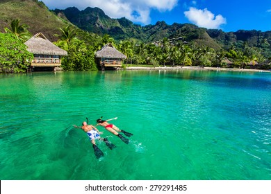 Young couple snorkeling over reef next to resort on a tropical island with over-water villas - Powered by Shutterstock