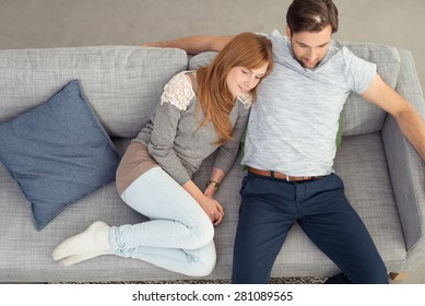 Young Couple Spending A Relaxing Day Together At Home Snuggling Up Close On A Large Comfortable Sofa With A Smile Of Contentment, High Angle View