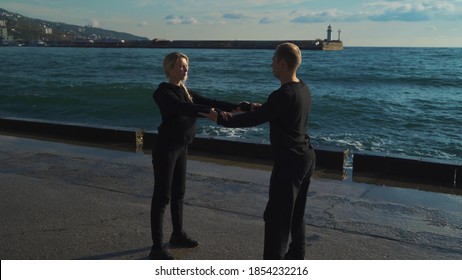 Young couple in sportswear are engaged in morning exercises against the background of the sea. The guy and the girl go in for sports together.