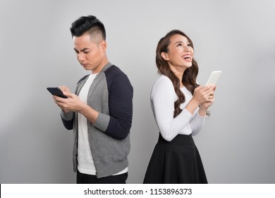 Young Couple Standing Back To Each Other And Looking At The Phone While Man Is Sad And Woman Is Excited.