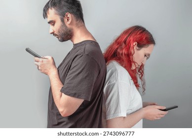 Young couple standing back to back using smartphones, symbol of emotional distance, relationship tension and lack of communication in modern everyday life.