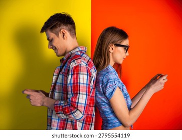 Young couple standing back to back using smartphones on colorful studio background.