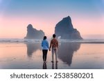 Young couple standing with holding hands enjoying the Wharariki beach and Archway islands on Tasman sea in West of Cape Farewell, New Zealand