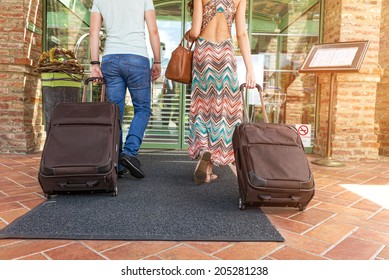 Young couple standing at hotel corridor upon arrival, looking for room, holding suitcases