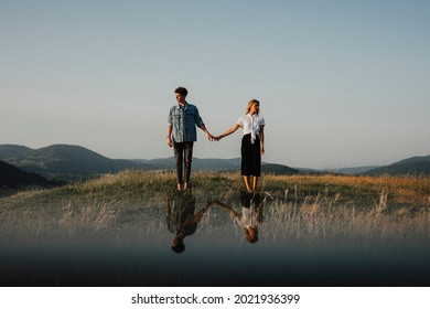 Young couple standing in nature in countryside, holding hands but looking away from each other.