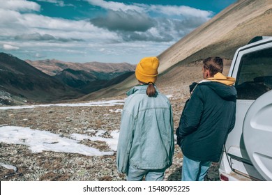 Young Couple Standing Near 4x4 Vehicle And Enjoying View Of Mountains. Winter Offroad Trip On Rental Car To Wild Nature.