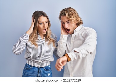 Young Couple Standing Over Blue Background Looking At The Watch Time Worried, Afraid Of Getting Late 