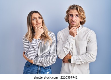 Young Couple Standing Over Blue Background Thinking Worried About A Question, Concerned And Nervous With Hand On Chin 