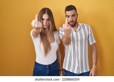 Young Couple Standing Over Yellow Background Showing Middle Finger, Impolite And Rude Fuck Off Expression 