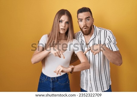 Young couple standing over yellow background in hurry pointing to watch time, impatience, upset and angry for deadline delay 