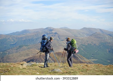 Young couple standing together on the mountain summit enjoying beautiful open view in nature during hiking travel. Hiking gear/equipment. Man and woman using trekking sticks.