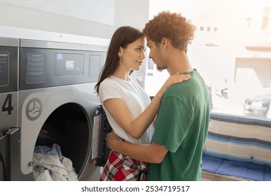 A young couple stands closely together inside a laundromat, gazing into each other's eyes while enjoying an intimate moment amid the machines and laundry. - Powered by Shutterstock