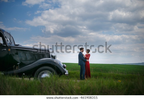 Young couple\
stands in the front of vintage\
car