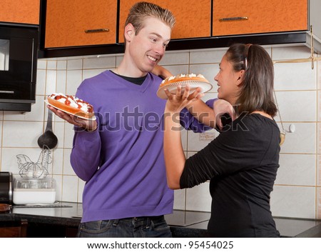Young couple starting a fight with cream pies in the kitchen