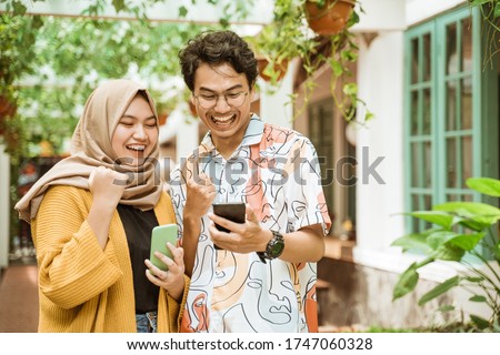 young couple stood laughing when they saw the cellphone