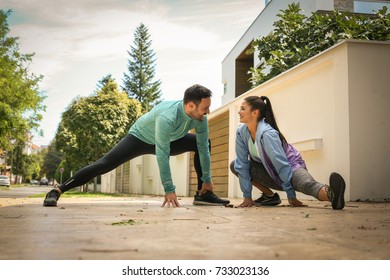 Young Couple Stretching On The Sidewalk After Running. Two People Exercises Together. 