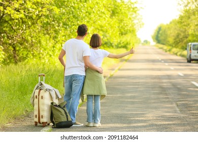 Young couple with suitcase hitchhiking on road