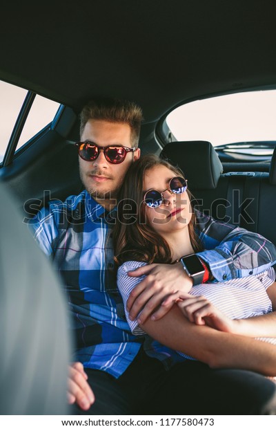 Young couple with sunglasses resting in the backseat\
of the car