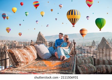 Young couple at sunrise on a rooftop in Cappadocia with hot air balloons in the background. Couple travels the world. Hot air balloon flights.