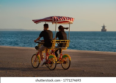 Young couple at sunset riding a four-wheeled bicycle (surrey bike) at promenade close to the sea. 