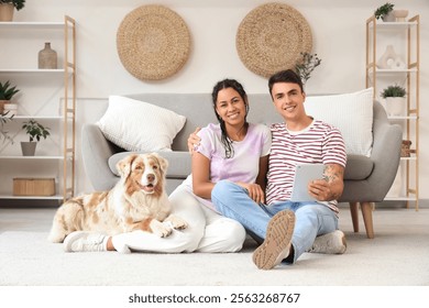 Young couple with tablet computer and cute dog sitting on floor at home