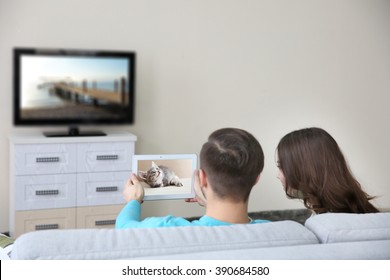 Young Couple With Tablet Watching And Taking Video From The TV At Home