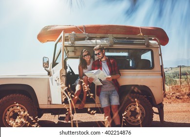Young couple taking a break to look at a map while on a roadtrip. Young man and woman on country road looking for directions on map.