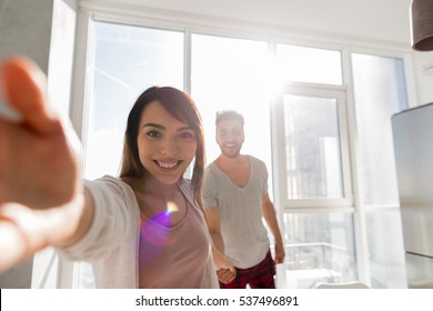 Young Couple Taking Selfie Photo Holding Hands In Kitchen, Asian Woman Leading Hispanic Man Modern Apartment With Big Windows Interior - Powered by Shutterstock